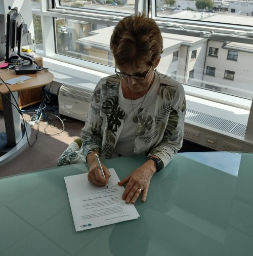 Principal sitting at a glass desk in her office, signing a document
