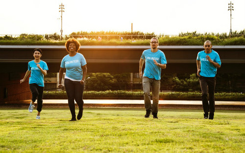 Four figures in blue T shirts running across a sports field
