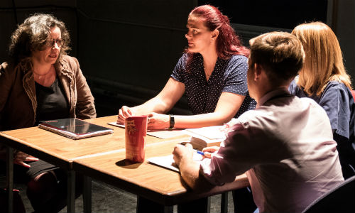 The play Cracks being performed, four actors in discussion around a table 