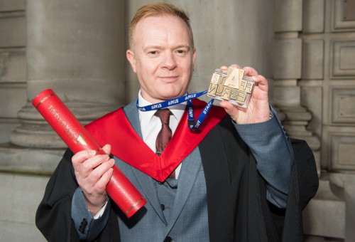 David Easton with his degree scroll and printed badge with the phrase 'staff nurse'