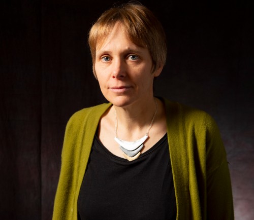 Portrait photo of Emma Hart, wearing black top and green cardigan, against a dark backdrop 