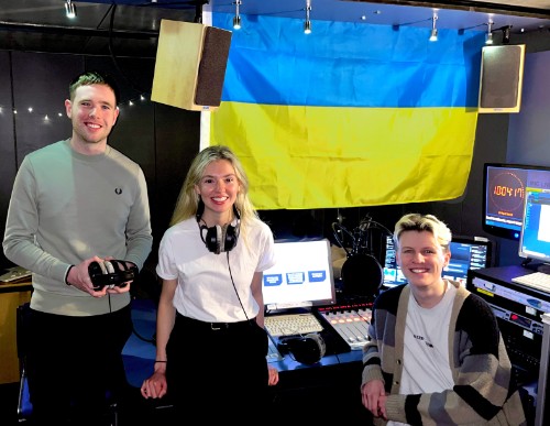 Three students in radio recording studio with Ukrainian flag in the background