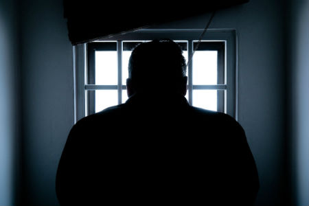 Silhouette of man's back in front of barred window