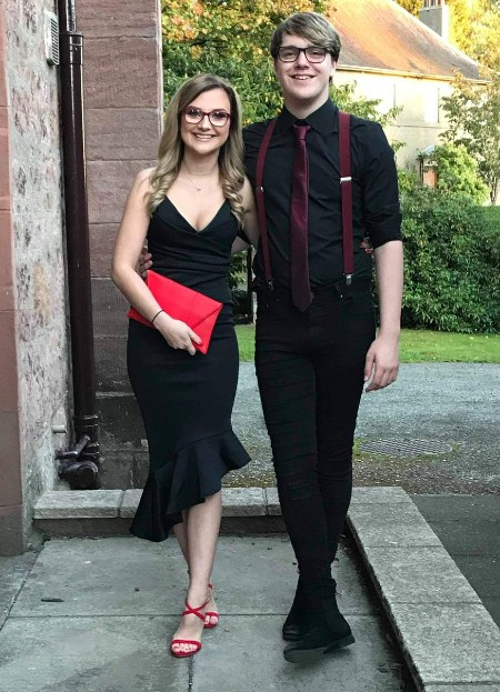 Kate, bespectacled and in dark dress, side by side with her taller brother Calum, also dressed in dark clothing  