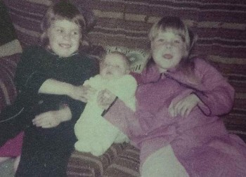 Kerri and Colene as children; Kerri in a blue dressing gown, Colene as a baby and their other sister Kelli is in pink.