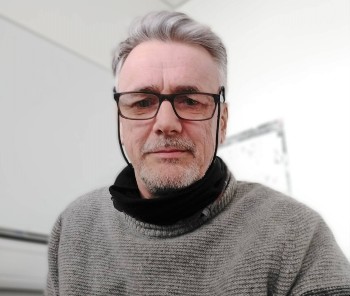Head of shoulders of Mark Dorris in grey top, wearing glasses