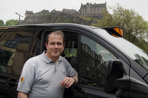 Matt Jones standing next to a taxi, with Edinburgh Castle in the background