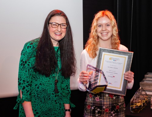 Close-up of two women, smiling, the one on the right clutching certificate and glass award