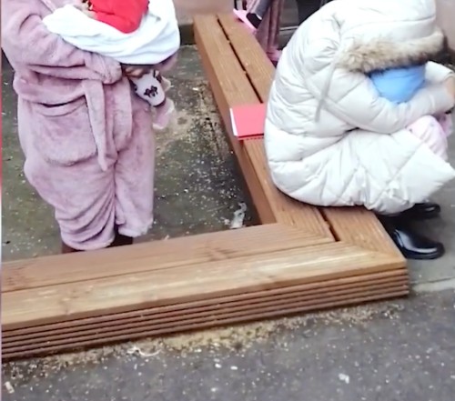 Two mothers with babies, wrapped against the cold and sitting on a wooden bench