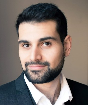 Head and shoulders of bearded, dark-haired Pavlos wearing dark jacket and open neck white shirt