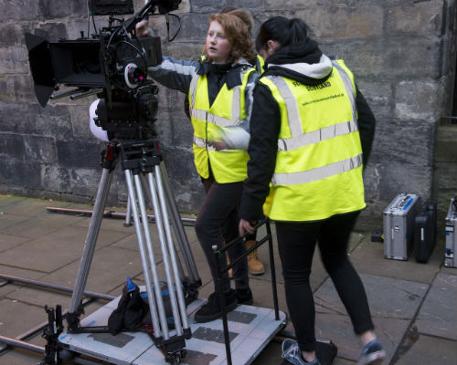 Two student filmmakers in high visibility gear working with a camera
