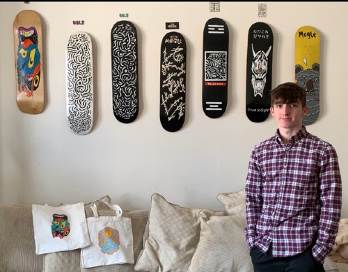 Matthew Porter in patterned shirt in front of his range of decorated skate boards