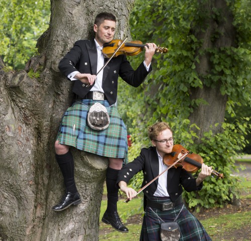 Thoren Ferguson sitting on sycamore tree and Lewis Kelly standing, both playing violins