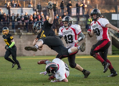 Action image of five kitted out American Football players on the pitch with spectators in the background