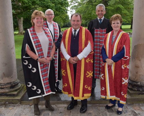 Will Whitehorn in ceremonial robes flanked on each side by two senior university figures against a woodland backdrop