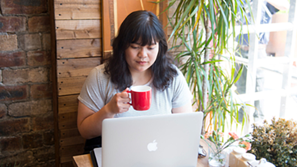 female presenting student with a cup of tea and a laptop in a cafe