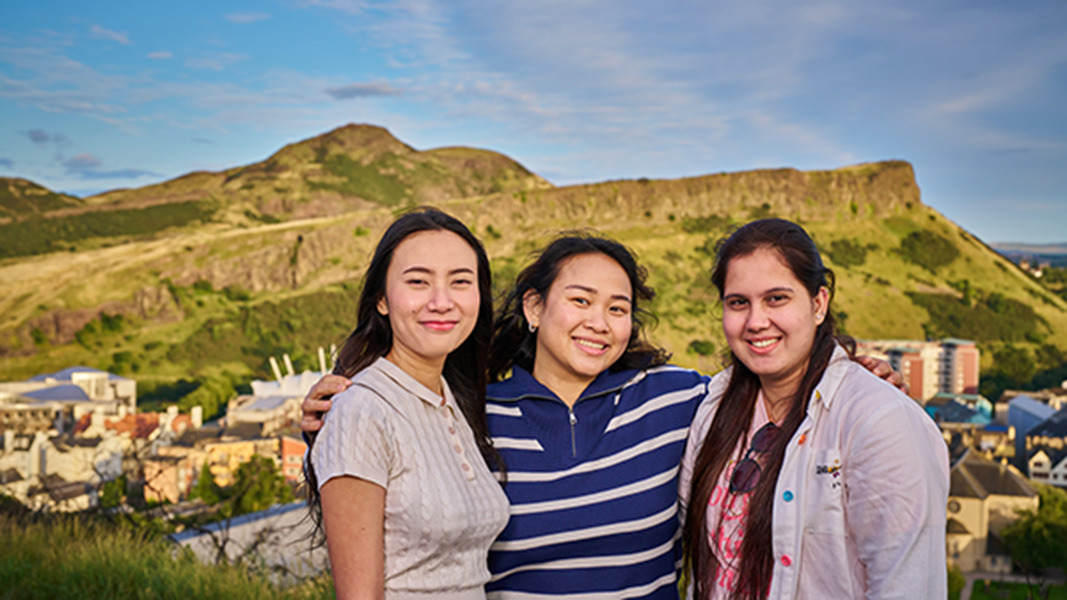 three smiling international students in front of Arthur's Seat