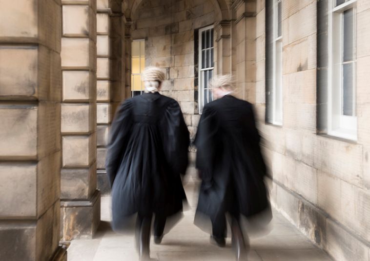 Two people wearing barrister robes and headgear walking away.