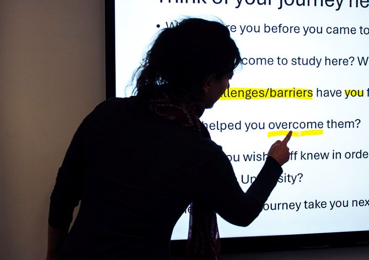 A person pointing at a screen displaying the word "overcome," underlined in yellow.
