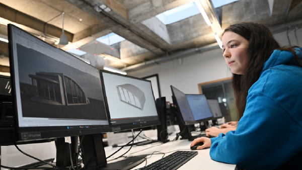 Person using computer-aided design software on multiple monitors in a digital design studio.