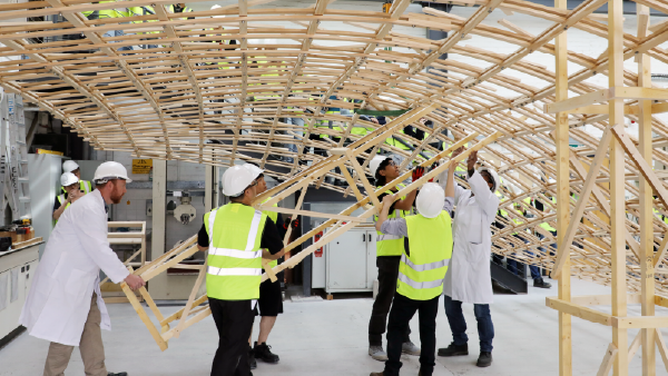 People in hard hats and high-visibility vests assembling a large timber framework in a workshop.
