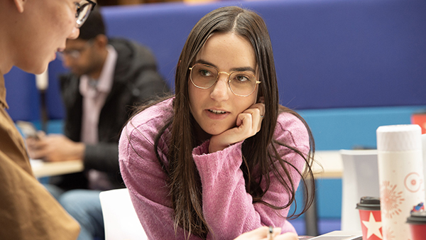 A student wearing glasses looks thoughtfully at another student