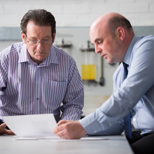 Two men looking at a piece of paper having a conversation.