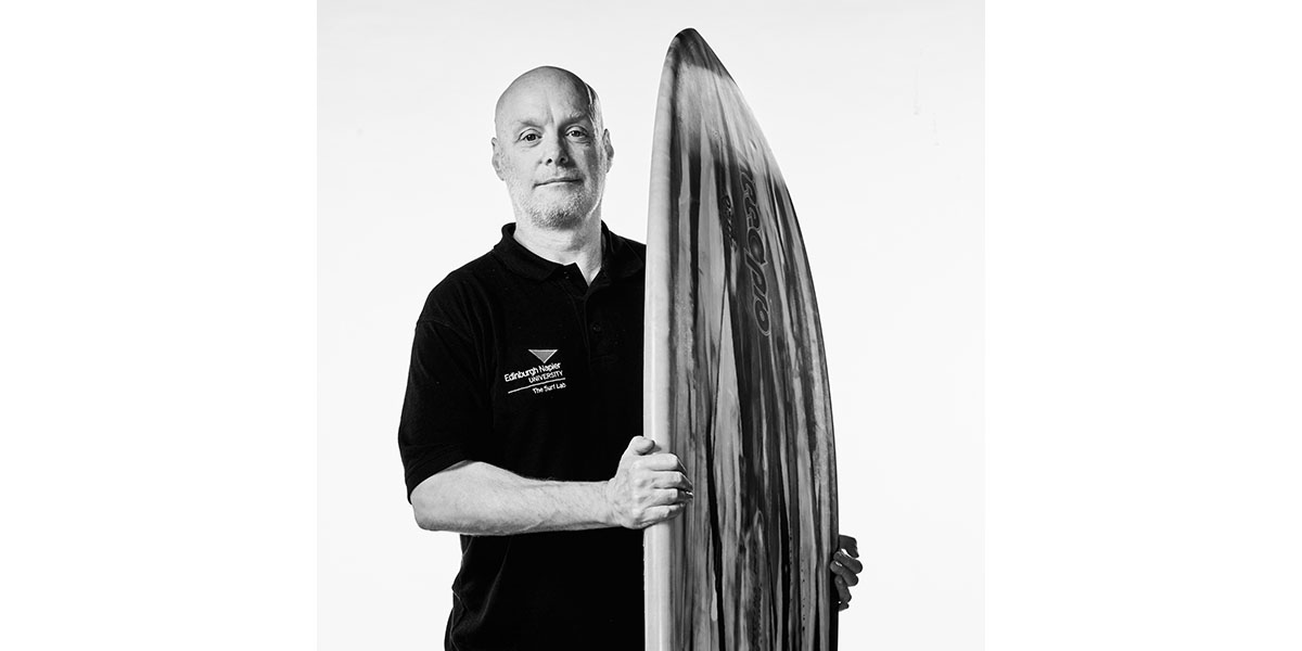 Dr. Brendon Ferrier, co founder of Edinburgh napier university's surf lab, stands confidently with his surfboard