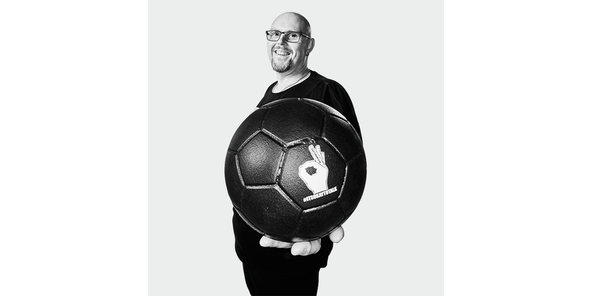 Ian housome holding an "ANDYS MAN CLUB" football that says "It's ok not to be OK"