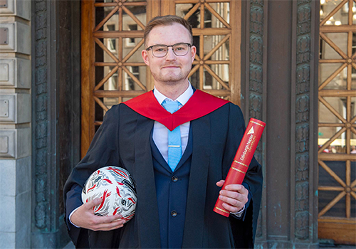 Neil Atkinson in graduation gown, holding football and Edinburgh Napier University scroll holder outside Usher Hall.