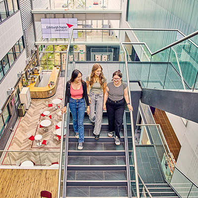 Three smiling students on the stairs in Sighthill's bright atrium