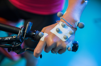 Hand with monitors attached, holding on to the bike handle bars, running a physical activity test.