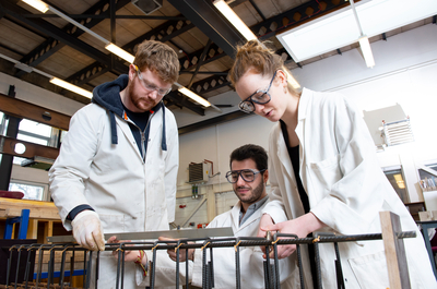 Engineering students wearing white lab coats, working on a practical project. 