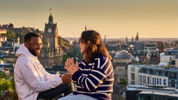 Two students chatting as Edinburgh city landscape is seen behind them 