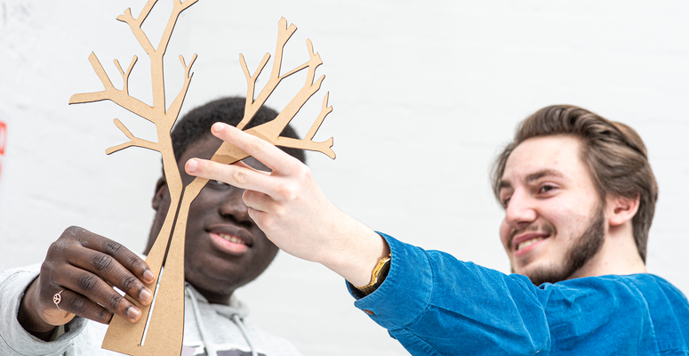 Two Creative Industries students holding up a cut-out of a tree