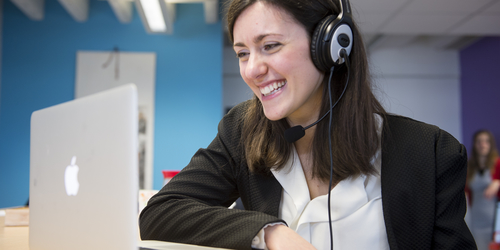 woman smiling next to laptop wearing headset